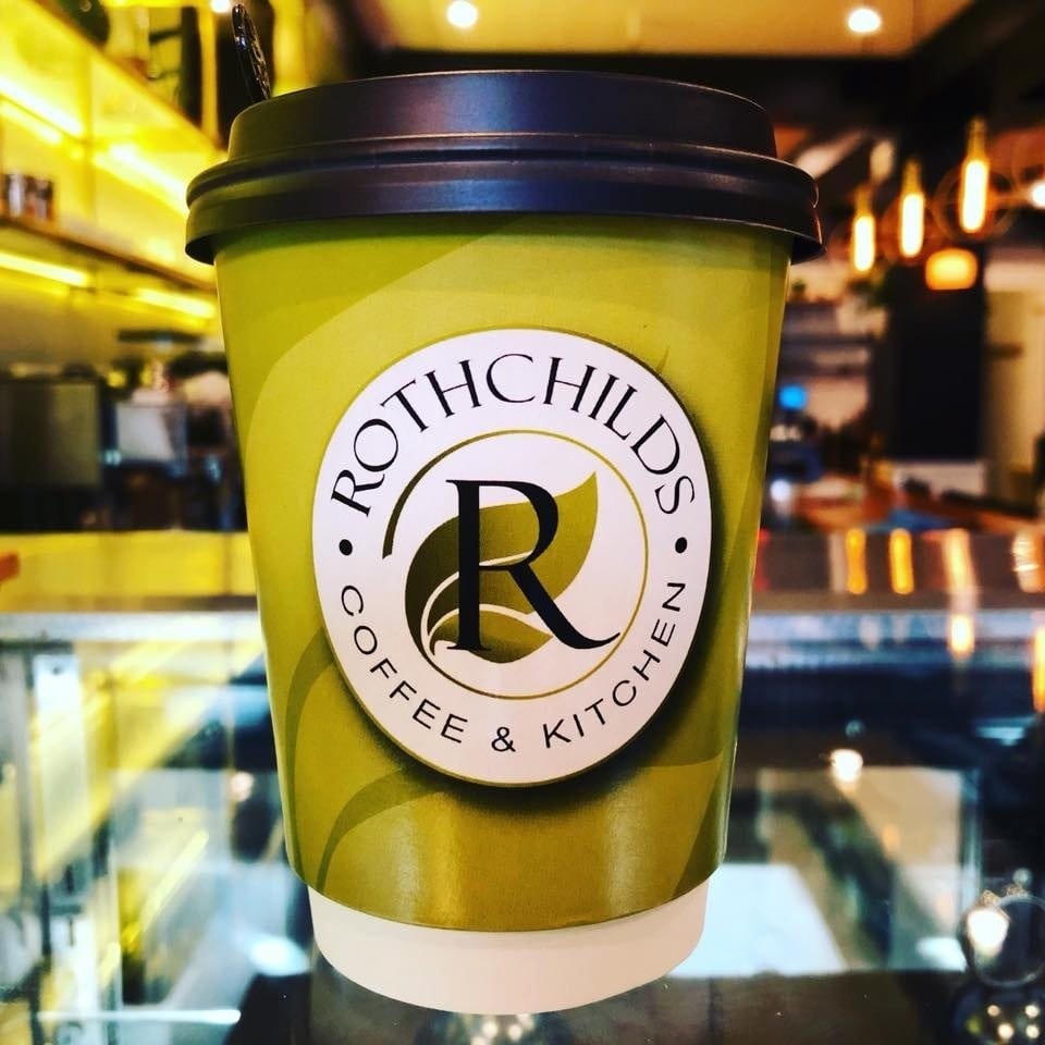Rothchilds Coffee & Kitchen branded cup with a black lid, against a blurred cafe background.