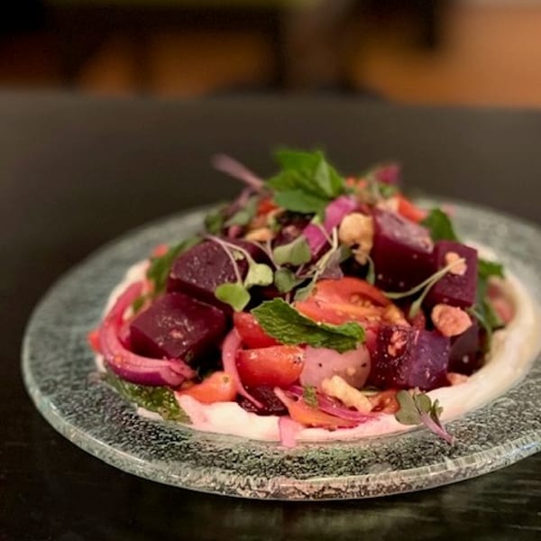 Vibrant beet and tomato salad with red onion, mint, and microgreens on a creamy base, served on a glass plate.