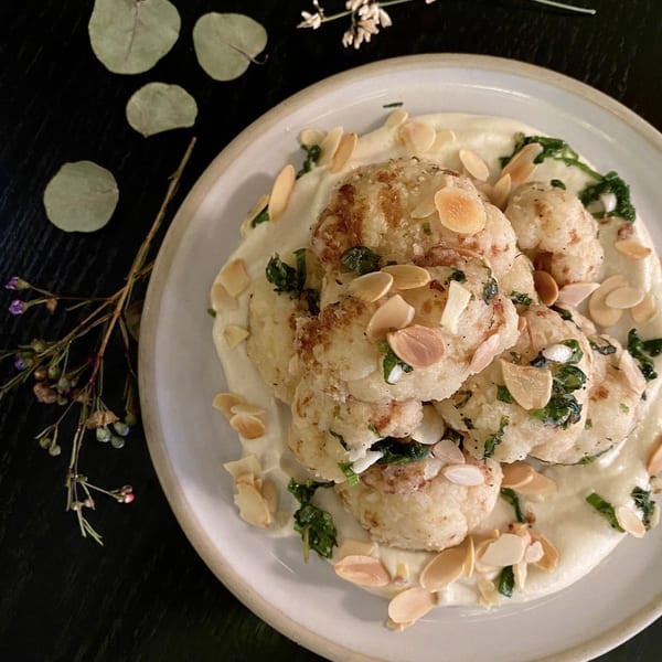 Roasted cauliflower florets with creamy sauce, fresh herbs, and sliced almonds on a white plate.
