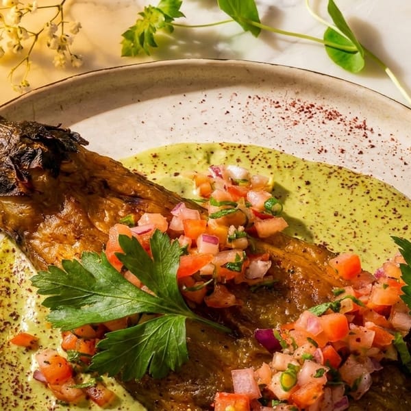Grilled eggplant with green sauce, fresh tomato and onion salsa, and parsley on a plate.