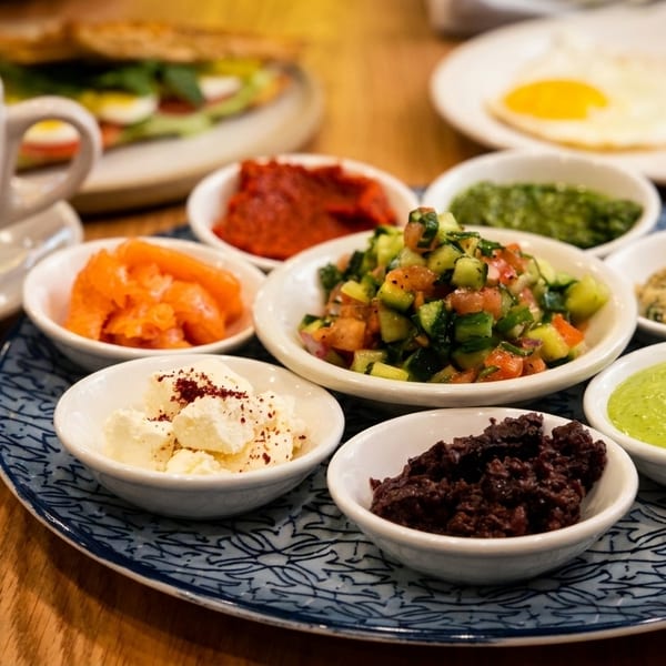 A breakfast spread with coffee, eggs, a sandwich, and small bowls of various dips and salads.