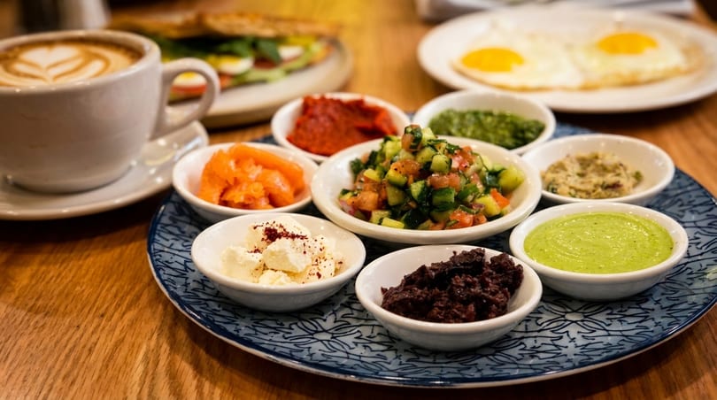 A breakfast spread with coffee, eggs, a sandwich, and small bowls of various dips and salads.