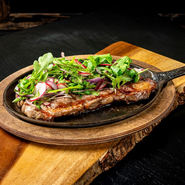 Grilled steak in a cast iron skillet, topped with fresh arugula, red onion, and radish slices.