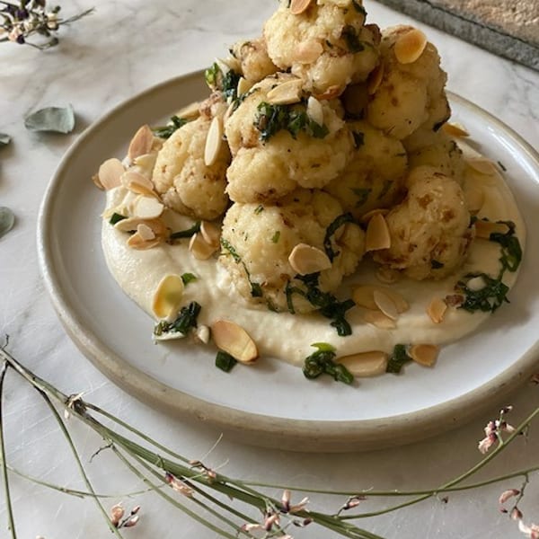Crispy cauliflower florets with herbs and sliced almonds, served on a bed of creamy white sauce.