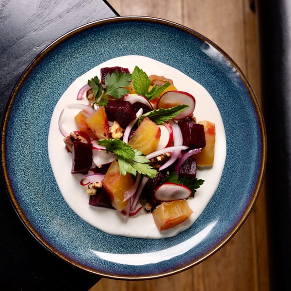Colorful beet salad with radishes, red onion, walnuts, and herbs on a creamy white sauce.